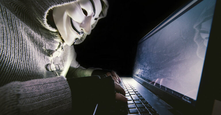 Masked criminal comitting a cyber crime at a computer