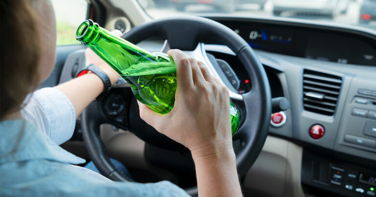 Person drivining and drinking a beer in a green glass bottle.