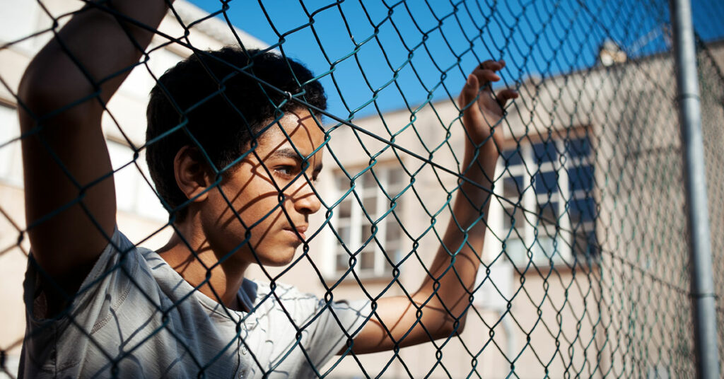 A boy looks while leaning up against a chain link fence
